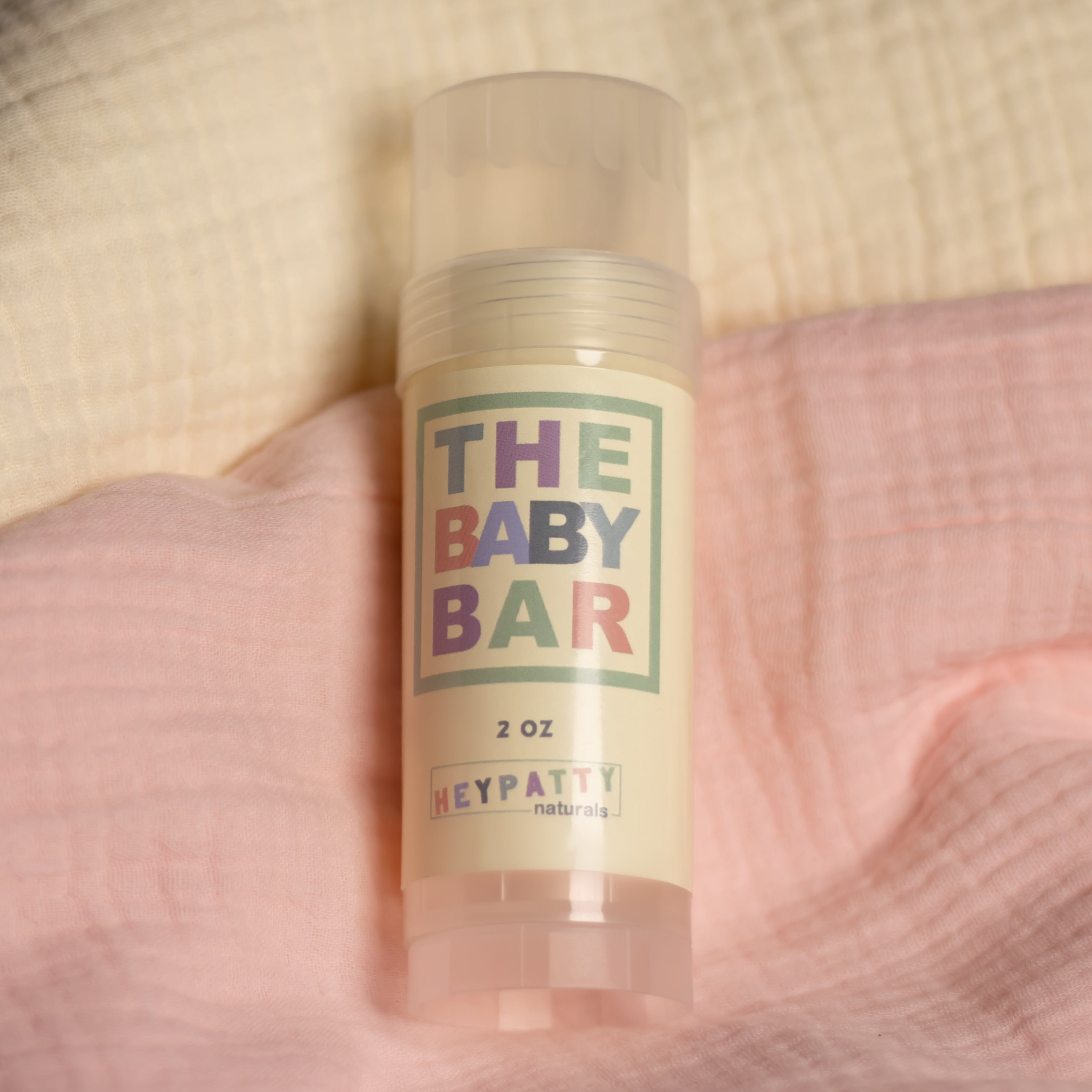 Bottle of 'The Baby Bar' by HEYPATTY Naturals on a soft pink fabric background